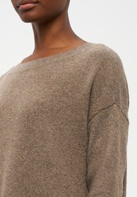 Sweater de malha castanho com um decote amplo, ombros caídos e uma textura macia. O design apresenta um corte descontraído e detalhes mínimos.