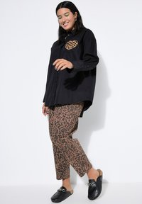 Black button-up shirt with a leopard print heart pocket, paired with brown leopard print pants and black slip-on shoes with a chain accent.