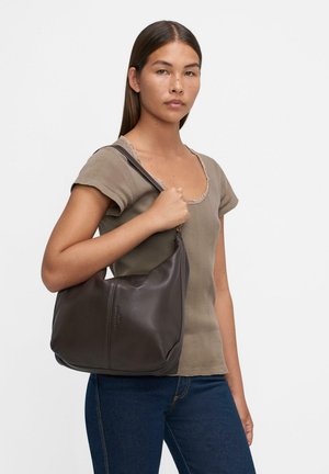 Brown leather shoulder bag with a smooth texture, curved shape, and zip closure; presented with a model wearing a fitted top and jeans.
