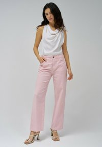 Pantalones de pierna ancha en rosa claro, confeccionados con una tela suave, que presentan un diseño clásico de cinco bolsillos y un cierre de botón. Combinados con una blusa blanca con drapeado.