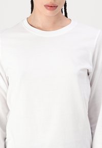 Langærmet hvid bomulds t-shirt med rund hals. Glat tekstur, tætsiddende form, minimal syning.