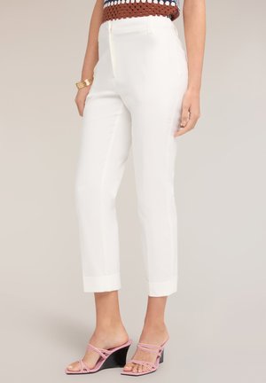 Białe, przycięte, dopasowane spodnie noszone z różowymi sandałami na koturnie z paskami oraz wielokolorowym topem bez rękawów, widoczne od talii w dół.