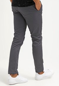 Pantaloni casual grigi realizzati in tessuto liscio, caratterizzati da un design slim fit, con cintura in vita e tasche frontali, abbinati a sneakers bianche.