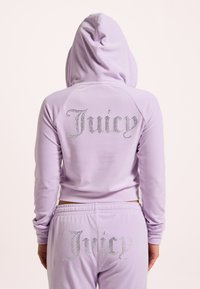 Felpa con zip lavanda e pantaloni coordinati con strass "Juicy" sul retro. Tessuto morbido, vestibilità rilassata, dettaglio con cappuccio e polsini a costine.