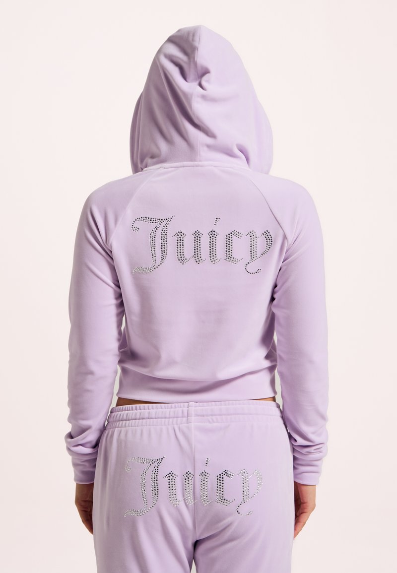 Felpa con zip lavanda e pantaloni coordinati con strass "Juicy" sul retro. Tessuto morbido, vestibilità rilassata, dettaglio con cappuccio e polsini a costine.