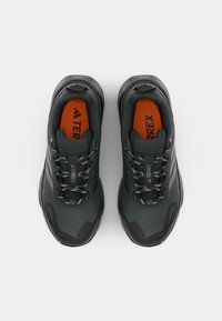 Schwarze Sportschuhe mit einer strukturierten synthetischen Oberseite, kontrastierender orangefarbener Innensohle und blau akzentuierten Schnürsenkeln. Verfügt über ein robustes Sohlendesign.