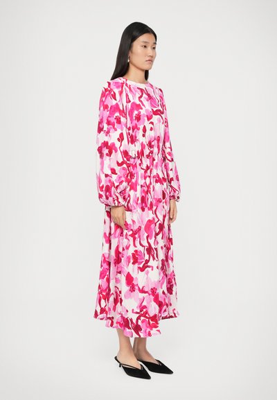Rochie lungă, florală, în nuanțe de roz și alb, cu mâneci tip balon, talie strânsă și margine fluidă. Asortată cu pantofi plat cu vârf ascuțit de culoare neagră.