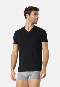 T-shirt noir à col en v en tissu doux, coupe ajustée, manches courtes ; associé à un boxer gris, posé sur un fond blanc.