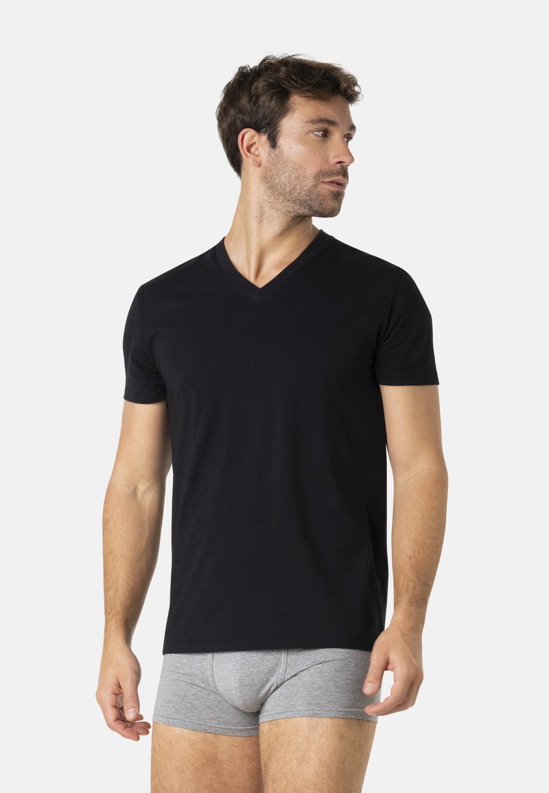 T-shirt noir à col en v en tissu doux, coupe ajustée, manches courtes ; associé à un boxer gris, posé sur un fond blanc.