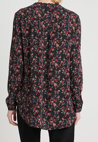 Svart långärmad skjorta täckt av ett blommönster med röda och gula blommor. Avslappnad passform, rundad nederkant och knappade manschetter.