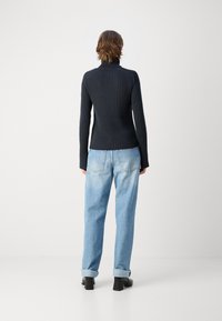 Maglione nero a coste con colletto alto abbinato a jeans in denim azzurro chiaro. I jeans sono a vestibilità comoda con orli risvoltati. Scarpe nere con tacco a blocco.