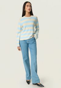 Stribet sweater i lyseblå og creme, ribbet tekstur, rund hals. Parret med lyseblå flagrende jeans og sorte spidse sko.