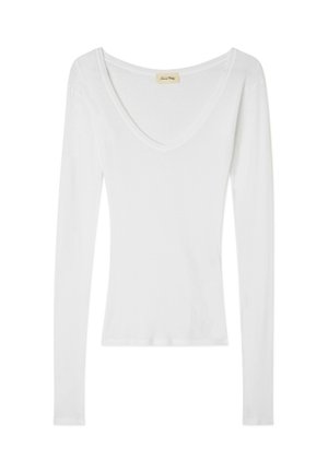 Haut long à manches blanches avec un col en V, fabriqué à partir d'un tissu doux et léger. Présente une silhouette ajustée avec des coutures minimales et sans embellissements.