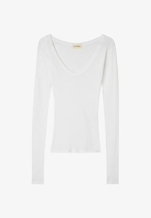 Balts garām piedurknēm krekls ar V veida kakla izgriezumu, izgatavots no mīksta, viegla auduma. Tam ir pieguļoša siluets ar minimāliem šuvēm un bez rotājumiem.