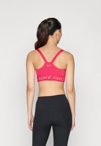 Roze sportski grudnjak s dizajnom leđa, s bijelim Nike logotipom i uzorak crnog pojasa. Uparen s crnim tajicama.