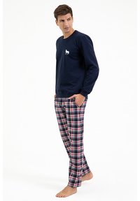 Granatowy sweatshirt z małym białym logo psa, zestawiony z czerwono-niebiesko-białymi spodniami w kratę. Materiał wydaje się być miękki i wygodny.