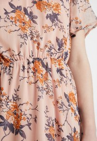 Blumenkleid aus leichtem Pfirsichstoff mit orangefarbenen und marineblauen Blumenmustern. Hat kurze Ärmel und einen elastischen Bund für eine lockere Passform.