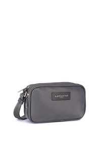Borsa da toiletry rettangolare grigia in tessuto liscio, con zip superiore e una tracolla laterale. Etichetta "LANCASTER PARIS" sul davanti.