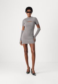 Robe grise courte avec une texture côtelée, dotée de manches courtes et d'un détail découpé. Associée à des gants longs gris et des talons hauts noirs.