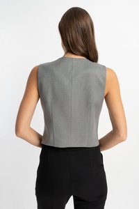Grauer ärmelloser Cropped-Top mit glatter Textur und strukturiertem Schnitt, mit Nahtdetails entlang des Rückens. Kombiniert mit schwarzen Hosen.