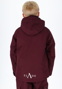 Giacca impermeabile color borgogna con cappuccio, con dettagli neri e logo bianco "SLADE" sul retro, tessuto testurizzato e forma slanciata.