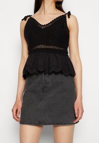 Top de ganchillo negro con tirantes ajustables y un dobladillo bordado en forma de ondas, combinado con una falda de mezclilla gris oscuro.