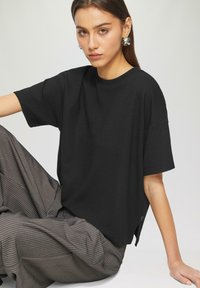 Zwart gestructureerd t-shirt met korte mouwen, ronde halslijn en zijsplitten, gecombineerd met grijs gestreepte wijde pantalons.