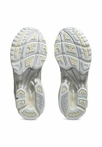 Suole di scarpe atletiche bianche con motivi in gomma testurizzata. Presentano bordi arrotondati, scanalature e un tallone rinforzato per supporto e trazione.