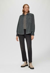 Vervaagde grijze langemouwen shirt met knopen aan de voorkant en een borstzak, gecombineerd met zwarte rechte jeans en beige enkellaarzen.