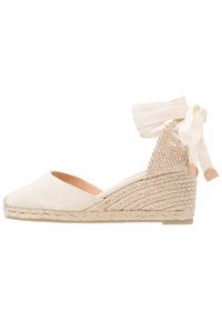 Beige lerret espadrille kile med en teksturert bakdel, kremfarget ankelbånd og flette av jute såle. Rundt tå med en liten hæl.