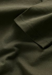 Close-up of dark green fabric showing a folded sleeve with visible stitching and soft texture.