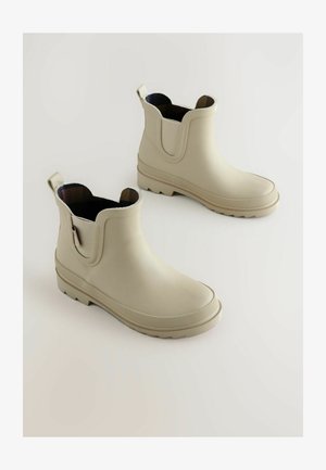 Botas de tobillo de goma beige con paneles laterales elásticos, suelas texturizadas y tiradores; exterior suave con acabado mate.