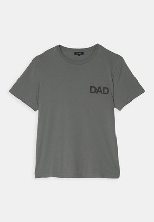 Harmaa puuvillapaita, jossa on tummaharmaina "DAD"-teksti, yhdistettynä vaaleansinisiin suoranlahkeisiin farkkuihin ja valkoisiin tennareihin, joissa on ruskeat pohjat.