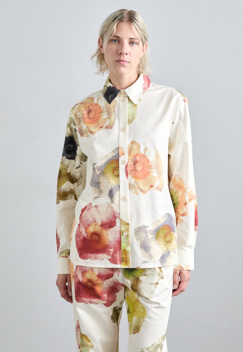 Camicia in cotone con stampa floreale in crema, caratterizzata da grandi fiori arancioni, rosa e neri. Presenta un collo e bottoni sulla parte anteriore.