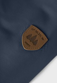 Tessuto blu navy con una toppa in pelle color miele raffigurante alberi in rilievo, cuciture dettagliate e il testo "N° 18.25 W NMT."