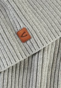 Écharpe grise en tricot avec texture côtelée, dotée d'une étiquette en cuir marron avec un logo. Le tissu semble doux et épais.