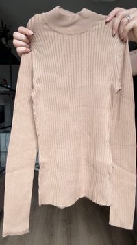 Camiseta de manga larga de canalé en color beige claro con cuello vuelto. Fabricada en una tela suave y elástica, presenta un bajo ligeramente desigual y un acabado texturizado.