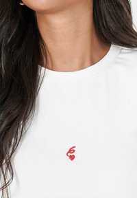 Witte katoenen t-shirt met een ronde hals en korte mouwen, voorzien van een klein rood geborduurd hartje op de linkerkant van de borst.