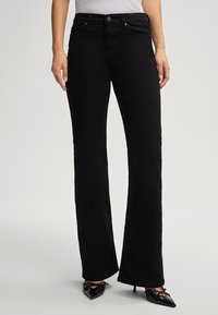 Zwarte flared jeans van katoen met een gladde textuur, voorzien van voorzakken, een knoopsluiting en een gemiddelde taillehoogte.
