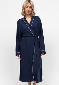 Accappatoio blu navy con maniche lunghe, caratterizzato da piping bianco lungo i bordi. Realizzato in tessuto morbido, include una cintura coordinata.