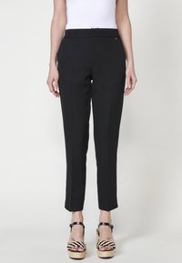 Pantalons noirs ajustés avec une coupe droite, présentant une finition en tissu lisse et des détails discrets sur les coutures latérales, associés à des sandales à plateformes noires et blanches imposantes.