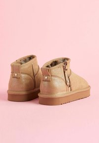 Botines de tobillo plateados con purpurina y textura suave, cremallera lateral y un tacón sencillo. Forro suave visible en la apertura. Suela de goma con tracción.