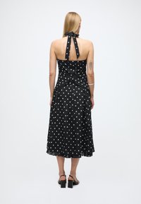 Vestido negro con lunares y cuello halter, cuerpo ajustado y falda fluida. Tejido texturizado y volantes delicados en el dobladillo.