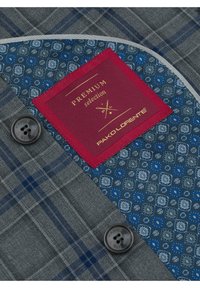 Szary materiał w kratę z niebieskimi akcentami, posiadający wzorzystą podszewkę i czerwoną metkę ze złotym napisem. Zawiera czarny guzik.