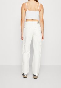 Vita cargo-byxor med lös passform, flera fickor och hög midja, kombinerat med en vit crop top och svarta sneakers med vita detaljer.