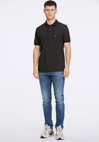 Polo nero a maniche corte, con colletto e un piccolo logo. Abbinato a jeans blu chiaro e sneakers crema con dettagli rossi.