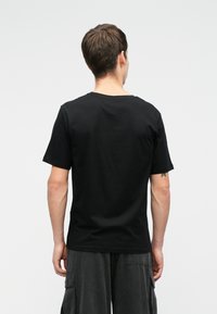 Černé bavlněné tričko s krátkým rukávem, kulatým výstřihem a volným střihem. Hladká textura s jednoduchým designem, bez viditelných log nebo vzorů.