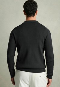 Pulover negru cu textură în vrac, cu design ajustat, gât rotund și mâneci lungi. Textură simplă și o culoare solidă, asortat cu pantaloni de culoare deschisă.
