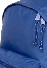 Marinblå ryggsäck med en texturerad nylonutsida, som har två robusta dragkedjor och flätade snören för enkel öppning.