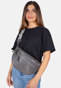 Sac banane en cuir gris avec une finition texturée, deux poches zippées et une sangle réglable à motifs, porté en bandoulière.